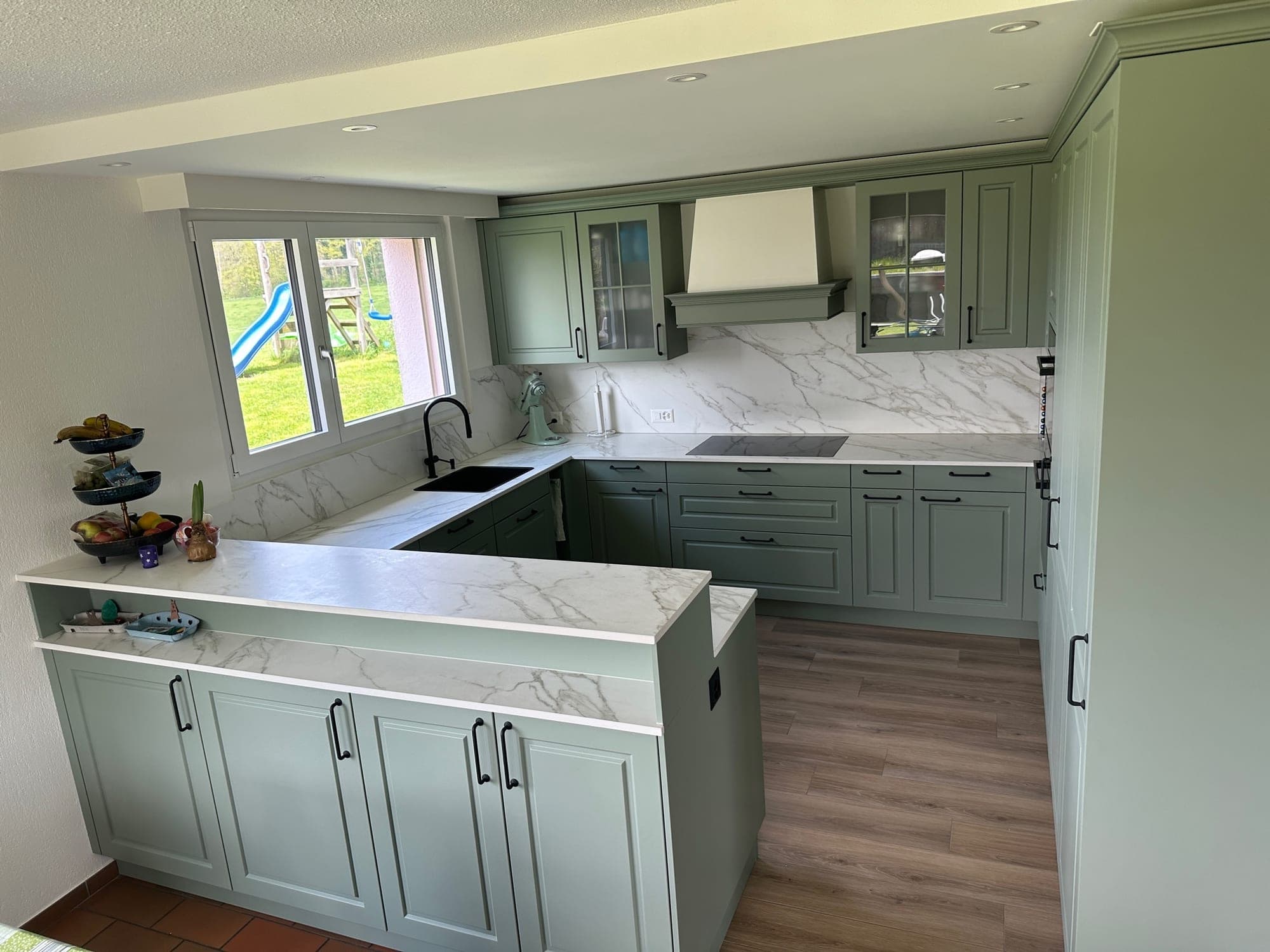 Landhausküche in Welsikon mit salbeigrünen Kassettenfronten und Arbeitsplatte in Marmoroptik